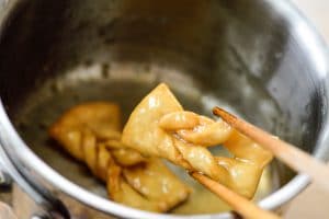 Deep-fried twisted ginger cookie dipped in a syrup held with chopsticks