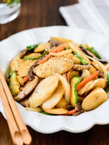 Korean oval size rice cakes stir-fried with beef, mushrooms, carrot, zucchini slices in a plate with chopsticks on the plate