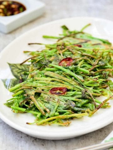 three small Korean watercress pancakes with a red chili pepper slice on top in a white plate with a dipping sauce on the side