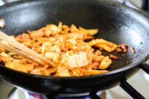 Stir-frying kimchi in a pan with chopsticks for bulgogi cheesesteak