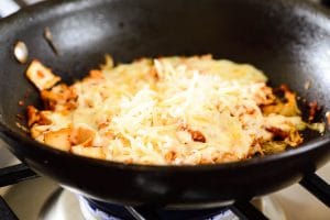 Stir-fried kimchi in a pan with melted cheese on top