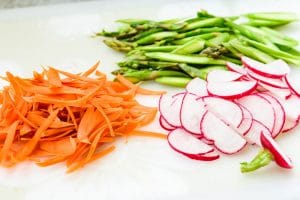 thinly sliced carrot, asparagus and red radish on a white cutting board