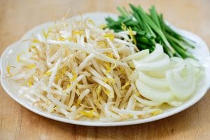 bean sprouts, thinly sliced onion and garlic chives on a white plate