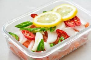 Slices of salmon, chili peppers, onion, and lemon in a rectangle glass container