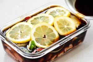 Soy sauce marinated salmon covered with lemon slices in a rectangle glass container