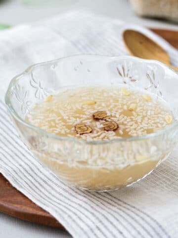 Korean rice drink in a glass bowl with floating grains of rice pine nuts and jujube slices