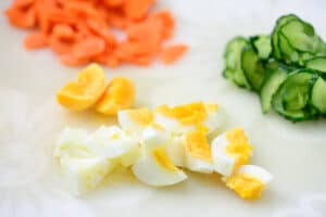 Dicing an boiled egg on a cutting board with sliced carrot and cucumber