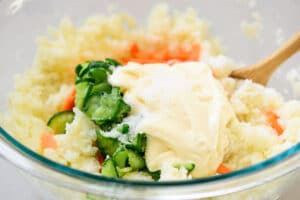 mixing mashed potatoes, sliced cucumber and carrot with mayonnaise and other seasoning ingredients