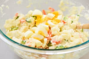 mixing mashed potatoes, sliced cucumber, carrot and egg with mayonnaise and other seasoning ingredients