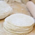 a stack of homemade dumpling wrappers on a wooden cutting board