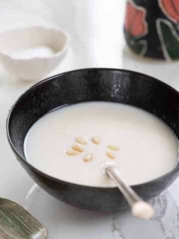Korean pine nut porridge in a black bowl with a spoon