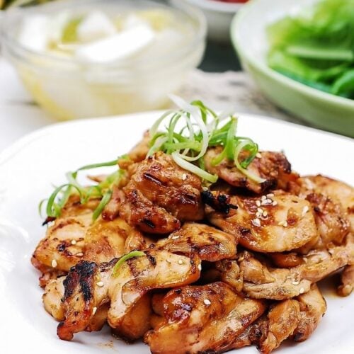 Chicken bulgogi on a plate with side dishes in the background