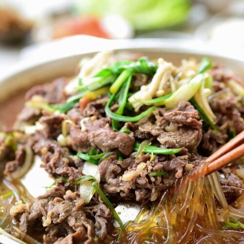 Bulgogi cooked on a Korean tabletop grill pan with glass noodles, scallions and enoki mushrooms