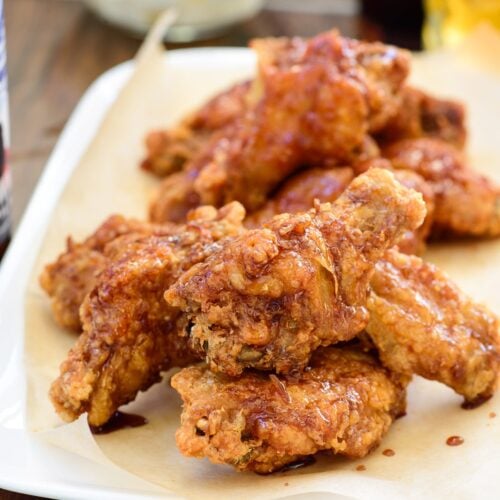 Korean fried chicken glazed with mild and spicy sauces served in a rectangle plate with beer and radish pickles