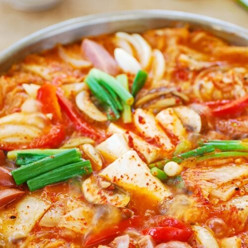 Korean Army stew with hot dog spam and bacon pieces in a large skillet